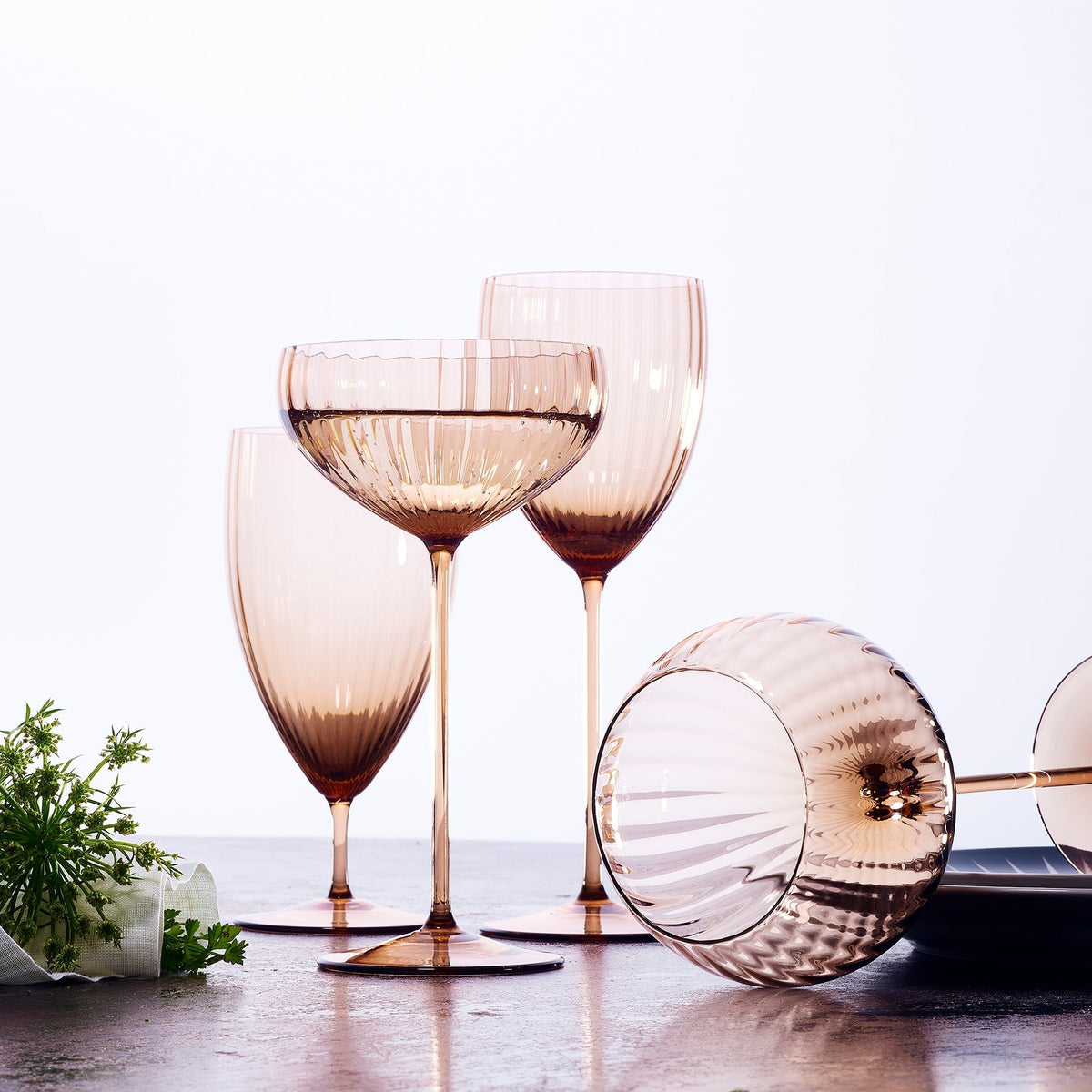 A Quinn Amber Coupe hand-blown glass by Caskata surrounded by additional shapes in the collection.