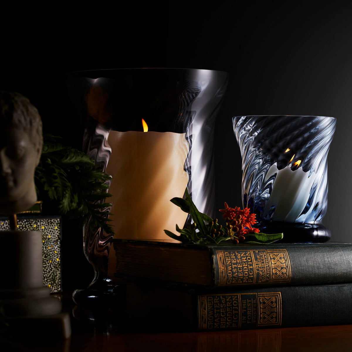 Quinn optic ocean votive candle by Caskata in lifestyle setting with stack of books and large hurricane.