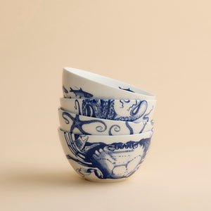 A set of four dishwasher-safe porcelain Coastal Icons Cereal Bowls, each decorated with blue illustrations of a crab, starfish, octopus, and fish.