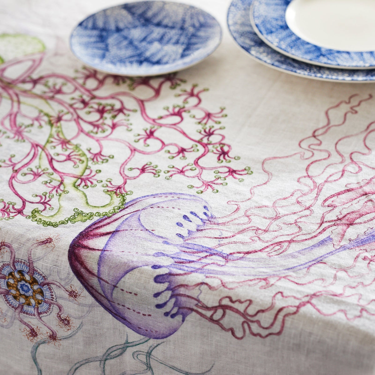 A playful blue and white Reef Hemp Tablecloth with embroidered jellyfish, showcasing colorful deep-sea dwellers by TTT.