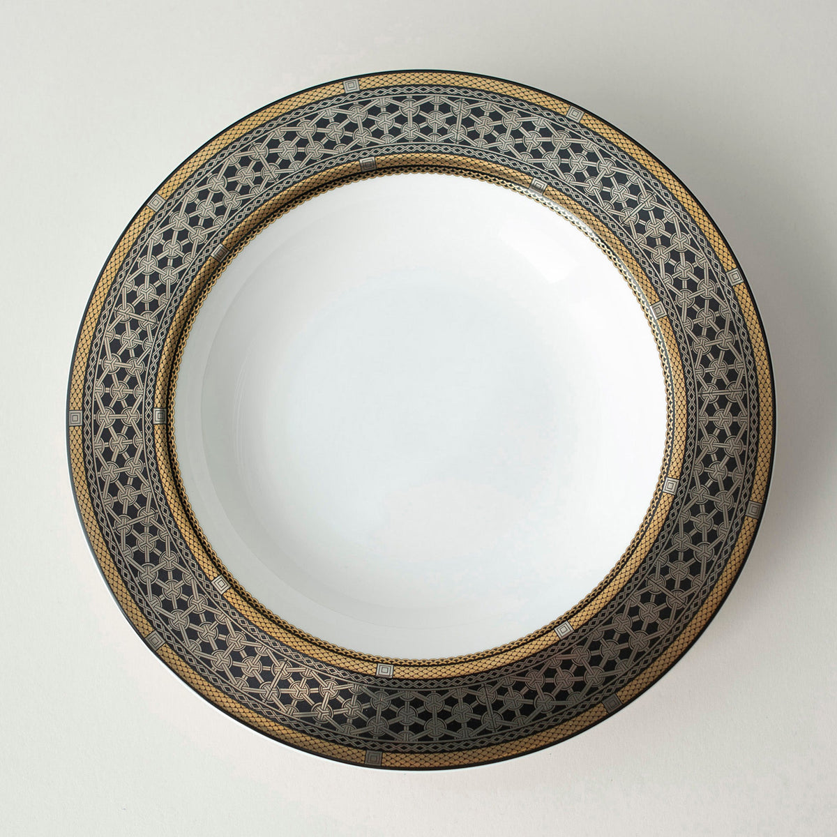 A Caskata Artisanal Home Hawthorne Onyx Gold &amp; Platinum Rimmed Soup Bowl on a sleek white surface.