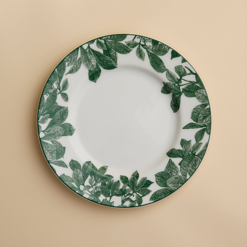 The Arbor Green Rimmed Salad Plate by Caskata, crafted from high-fired porcelain and featuring a green leafy pattern around the rim, is shown placed on a beige background.