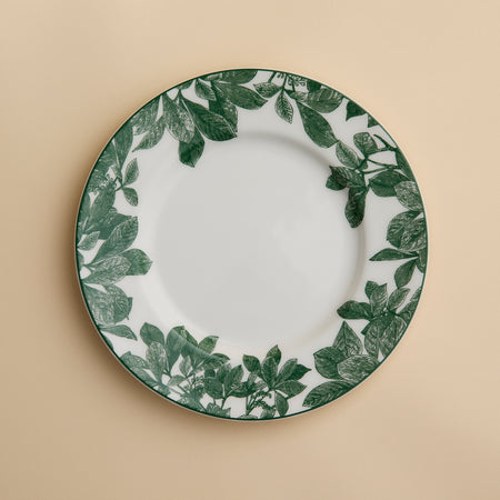 The Arbor Green Rimmed Salad Plate by Caskata, crafted from high-fired porcelain and featuring a green leafy pattern around the rim, is shown placed on a beige background.