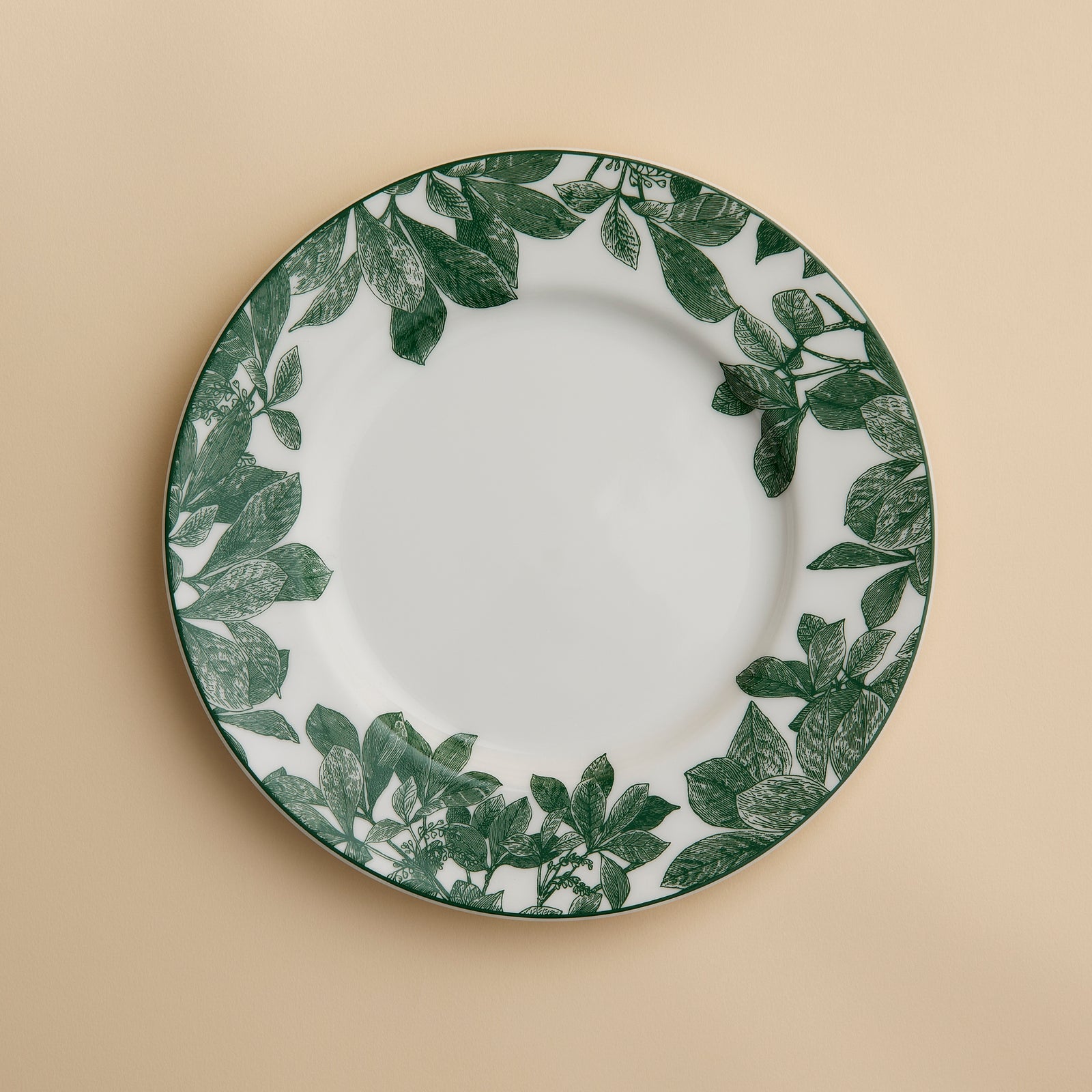 The Arbor Green Rimmed Salad Plate by Caskata, crafted from high-fired porcelain and featuring a green leafy pattern around the rim, is shown placed on a beige background.
