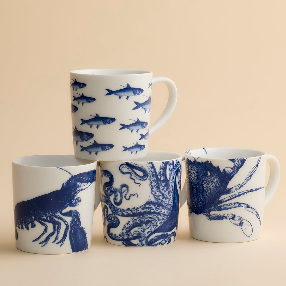 A set of four white ceramic Coastal Icons Mugs, each decorated with blue illustrations of a lobster, an octopus, a crab, and various fish.