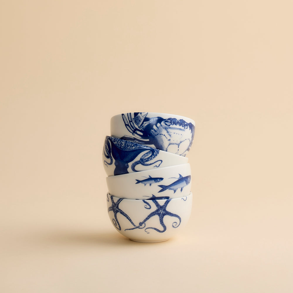 A stack of four Coastal Icons Snack Bowls, each decorated with a blue nautical illustration of a crab, octopus, fish, or starfish.