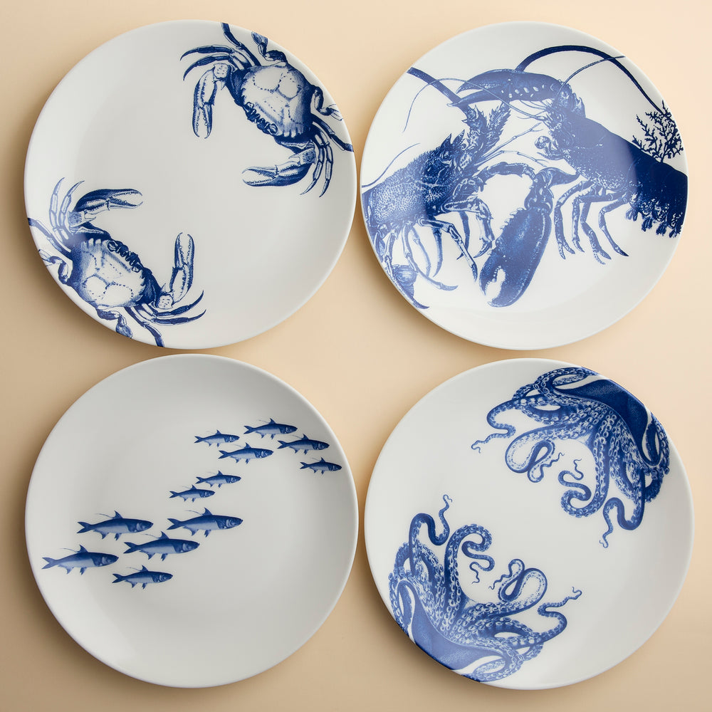 Four dishwasher-safe Coastal Icons Dinner Plates, Mixed Set of 4, each featuring blue illustrations of marine life: two crabs, two lobsters, a school of fish, and an octopus.