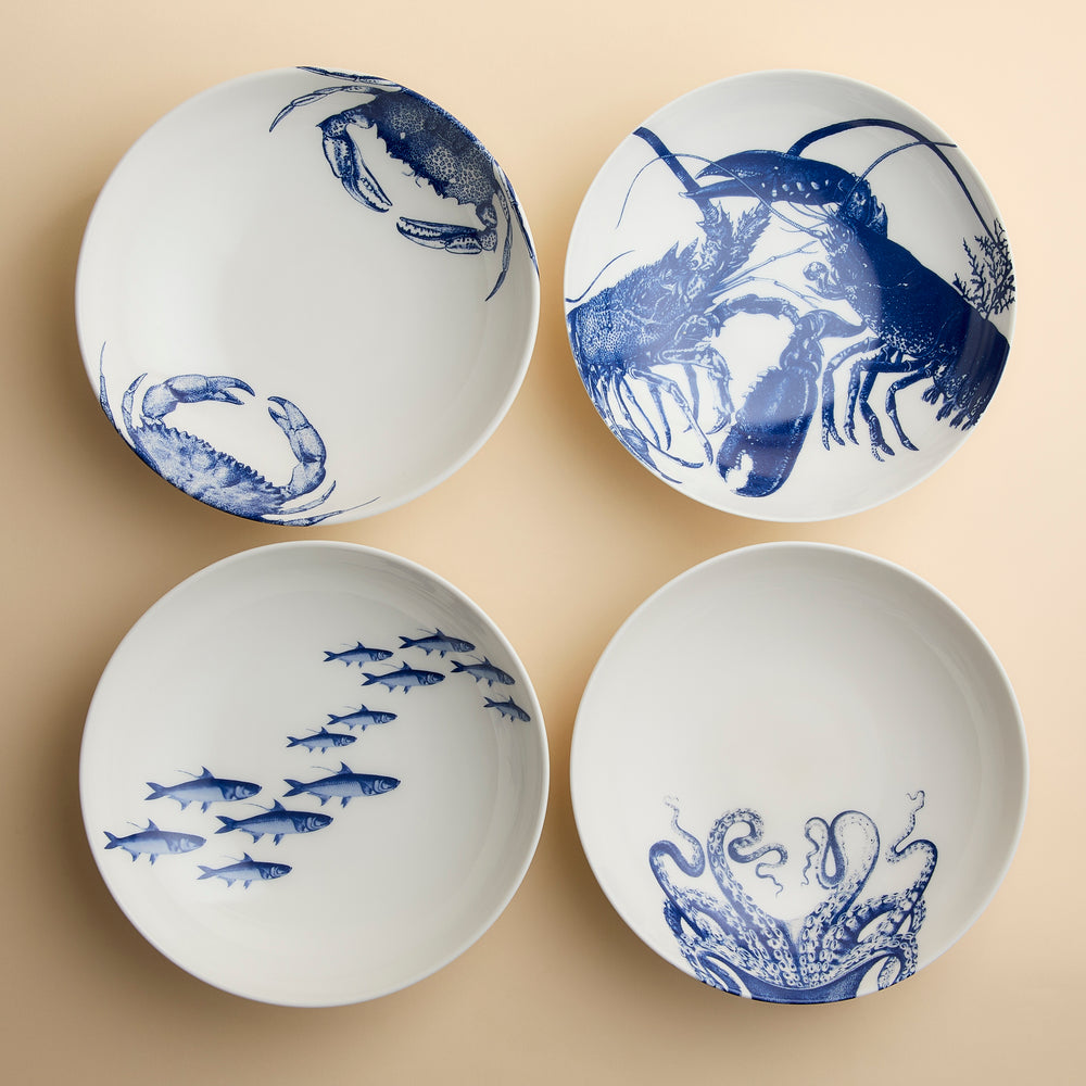 Caskata Coastal Icons Entrée Bowls, a set of four white porcelain bowls, each featuring a different blue marine life illustration: two crabs, a lobster, a school of fish, and an octopus.