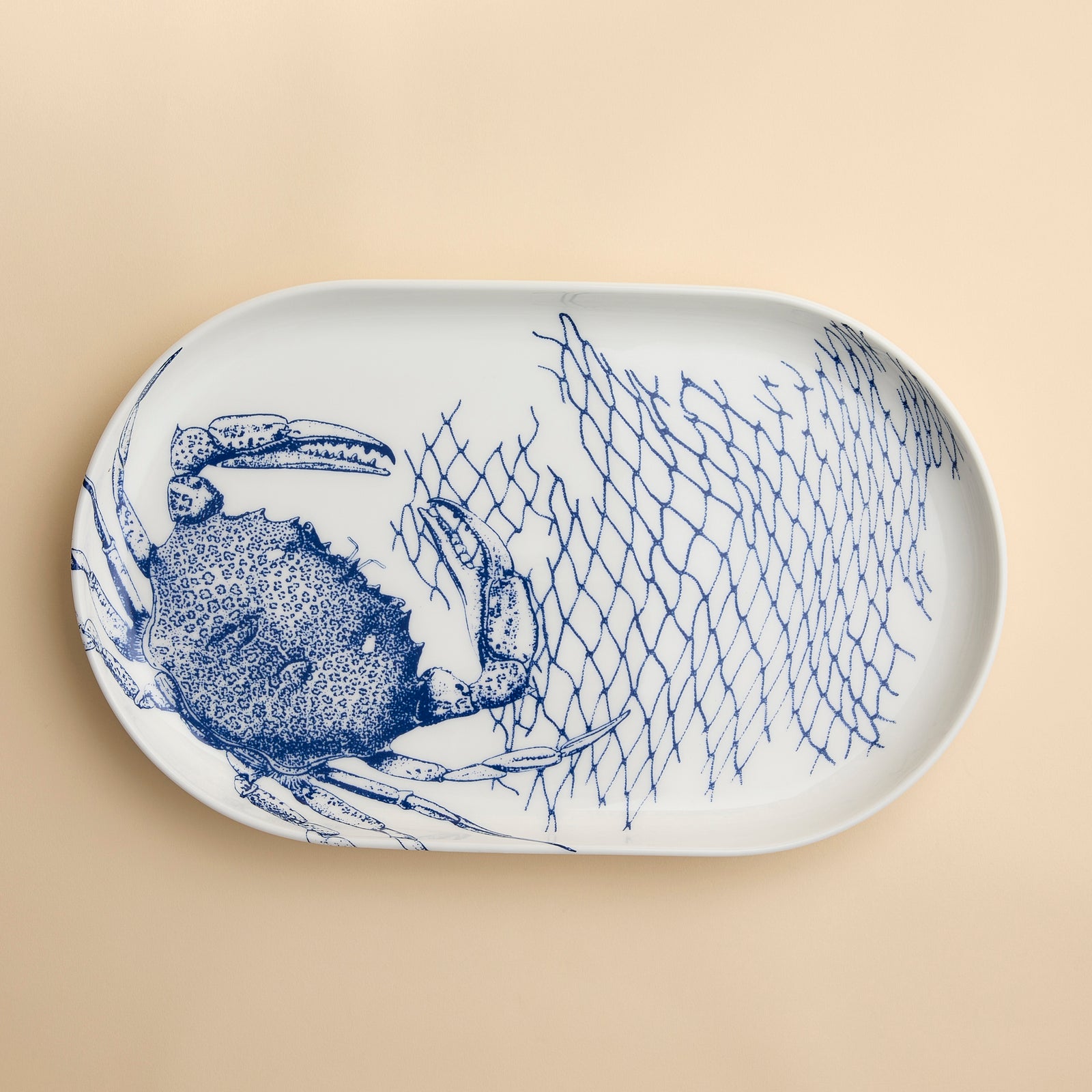 Crabs and nets sprawl across this contemporary coupe oval platter in blue and white high-fired porcelain from Caskata.