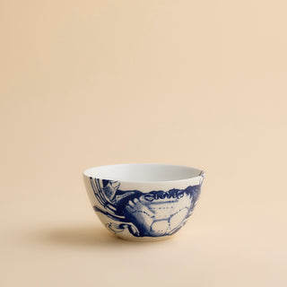 The Caskata Crab Cereal Bowl is a white ceramic bowl featuring a blue illustration of a crab on one side, displayed against a plain beige background.