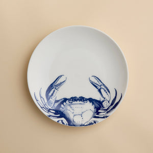 The Crab Coupe Salad Plate by Caskata Artisanal Home features a white porcelain design accented with a blue crab illustration on the lower half, making it a perfect addition to your coastal dinnerware collection for serving fresh salads or appetizers.