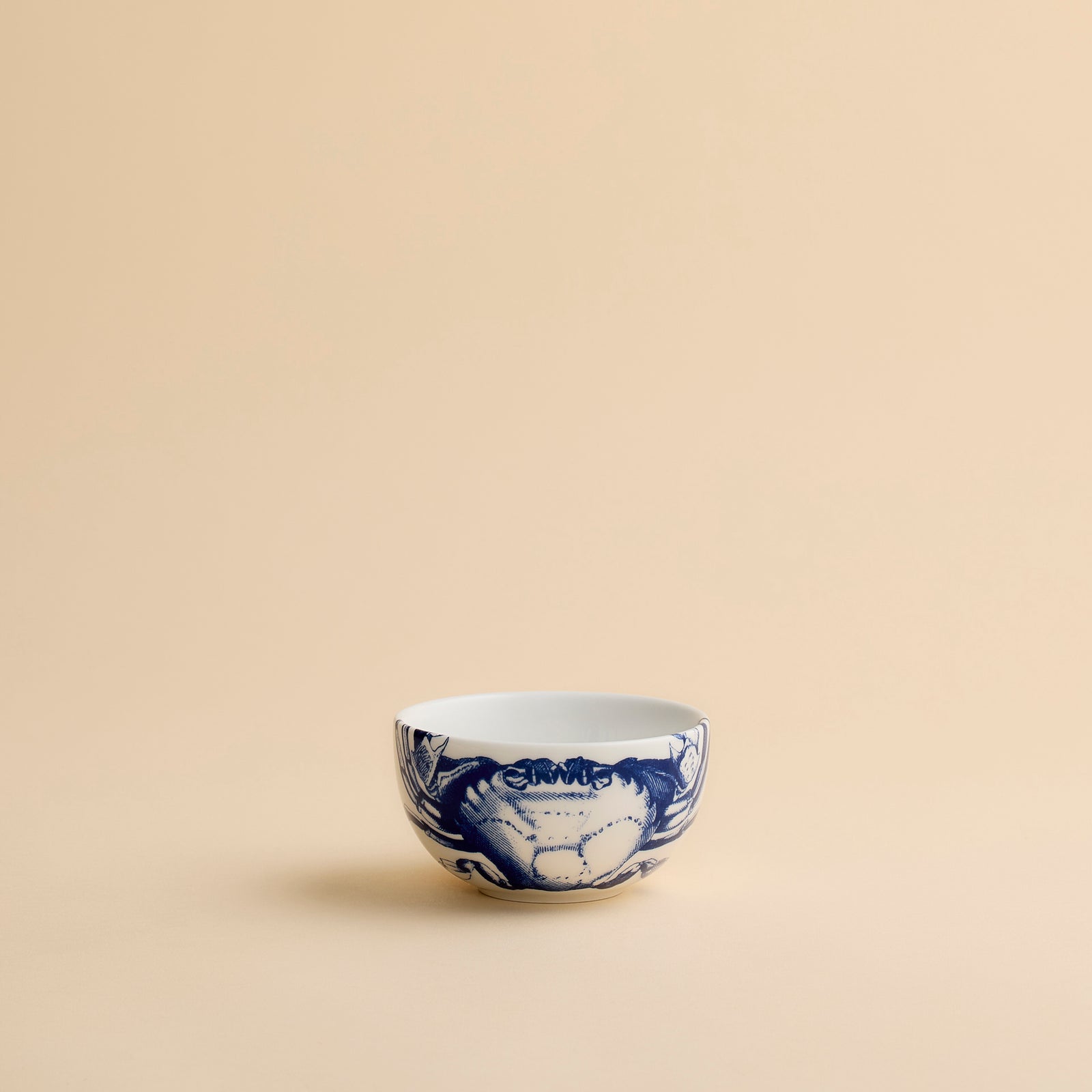 The Caskata Artisanal Home Crab Snack Bowl is a small coastal bowl featuring a blue crab design on the front, displayed against a simple beige background.