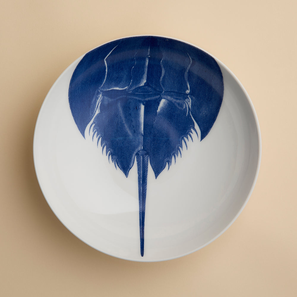 Caskata’s Horseshoe Crab Entrée Bowl—a white oval plate adorned with a blue horseshoe crab illustration viewed from above—adds exquisite coastal charm and seaside elegance to any table setting.