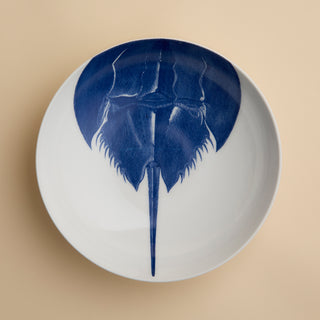 Caskata’s Horseshoe Crab Entrée Bowl—a white oval plate adorned with a blue horseshoe crab illustration viewed from above—adds exquisite coastal charm and seaside elegance to any table setting.