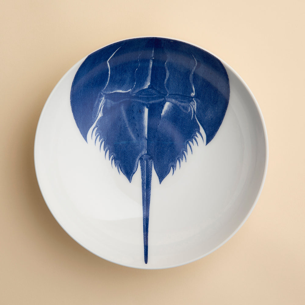 Caskata’s Horseshoe Crab Entrée Bowl—a white oval plate adorned with a blue horseshoe crab illustration viewed from above—adds exquisite coastal charm and seaside elegance to any table setting.