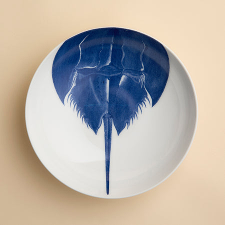 Caskata’s Horseshoe Crab Entrée Bowl—a white oval plate adorned with a blue horseshoe crab illustration viewed from above—adds exquisite coastal charm and seaside elegance to any table setting.