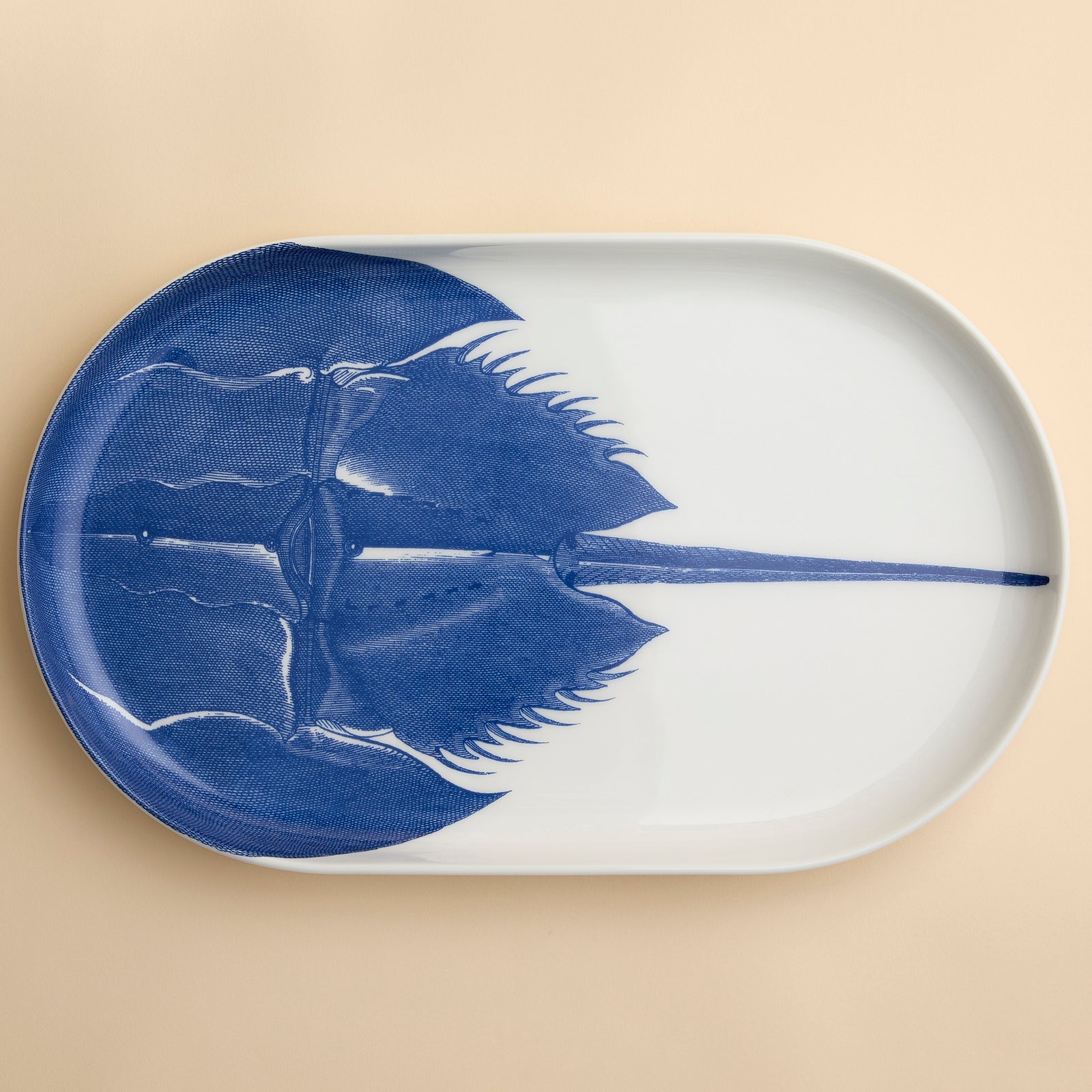 A highly detailed engraving of a horseshoe Crab in brilliant blue adorns this large oval platter from Caskata in premium porcelain, 