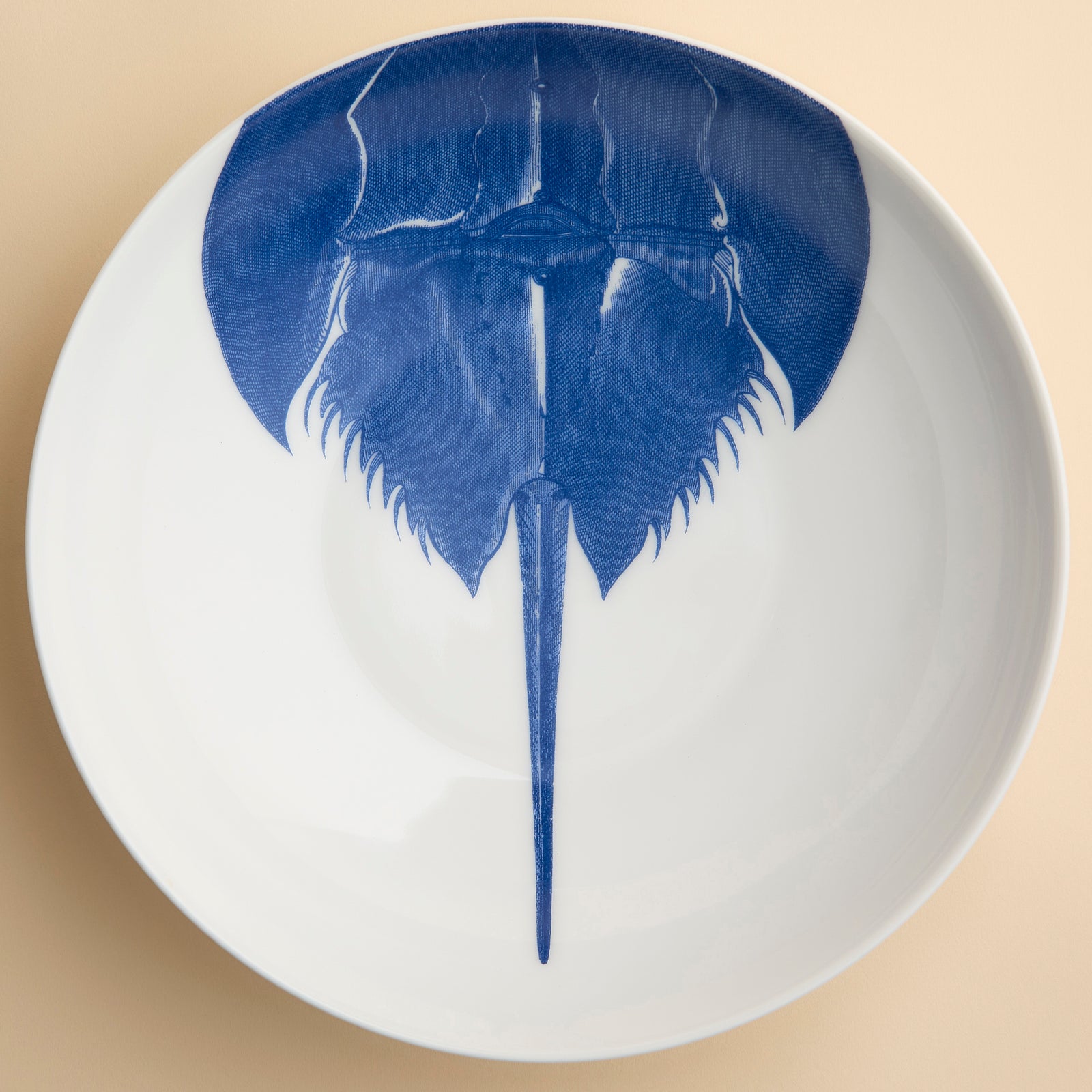 A highly detailed engraving of a horseshoe Crab in brilliant blue adorns this large serving bowl from Caskata in premium porcelain, seen from overhead.