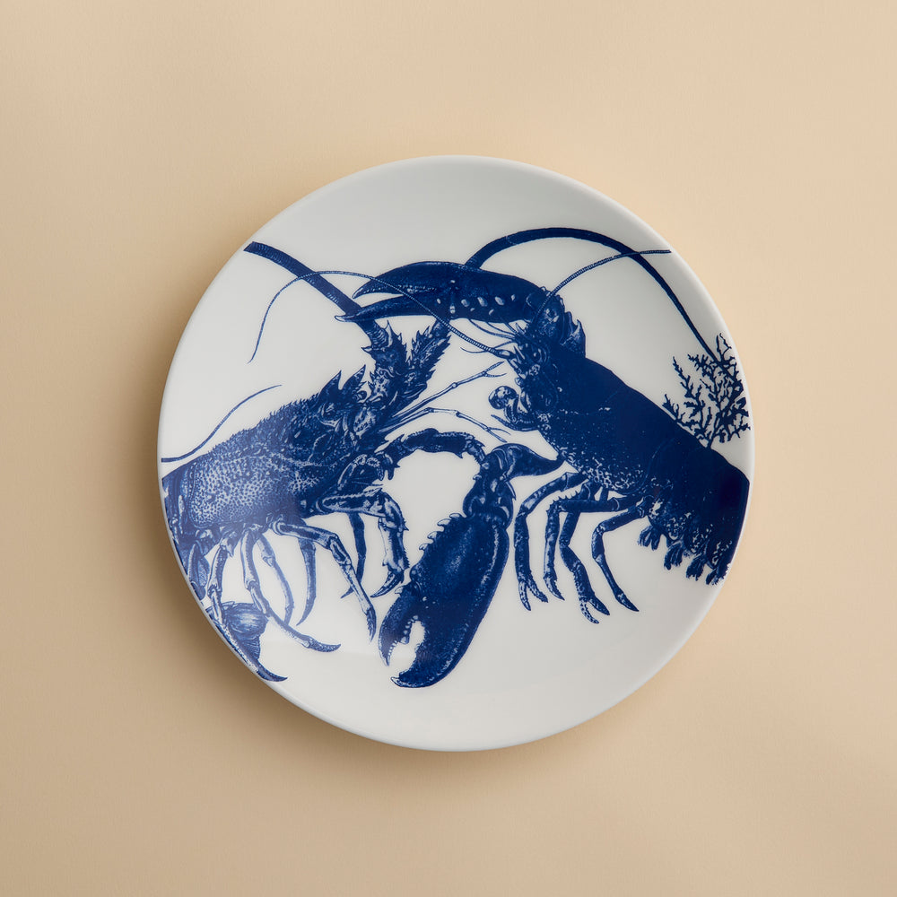 Add a coastal touch to your table with the Lobster Coupe Salad Plate by Caskata, crafted from white ceramic and showcasing a blue illustration of two lobsters facing each other on a subtle beige background—a delightful addition to any ocean-inspired dinnerware collection.