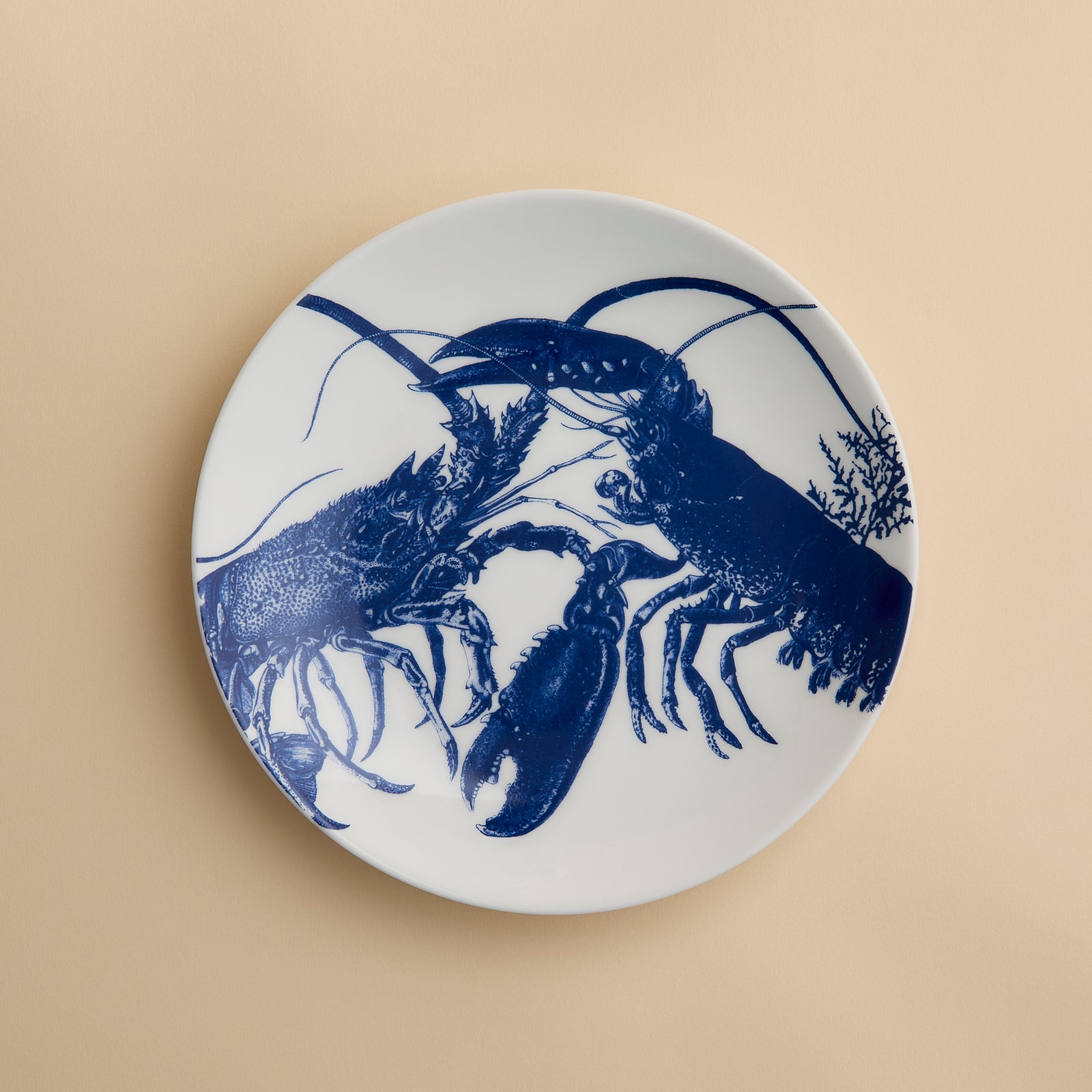 Add a coastal touch to your table with the Lobster Coupe Salad Plate by Caskata, crafted from white ceramic and showcasing a blue illustration of two lobsters facing each other on a subtle beige background—a delightful addition to any ocean-inspired dinnerware collection.