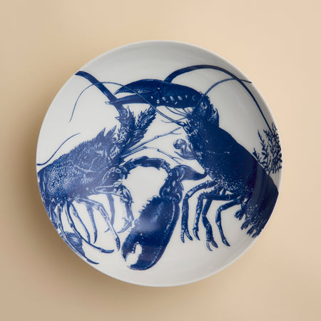 The Lobster Entrée Bowl by Caskata, from our coastal dinnerware collection, is a white ceramic bowl featuring a blue illustration of two lobsters facing each other on a beige background.