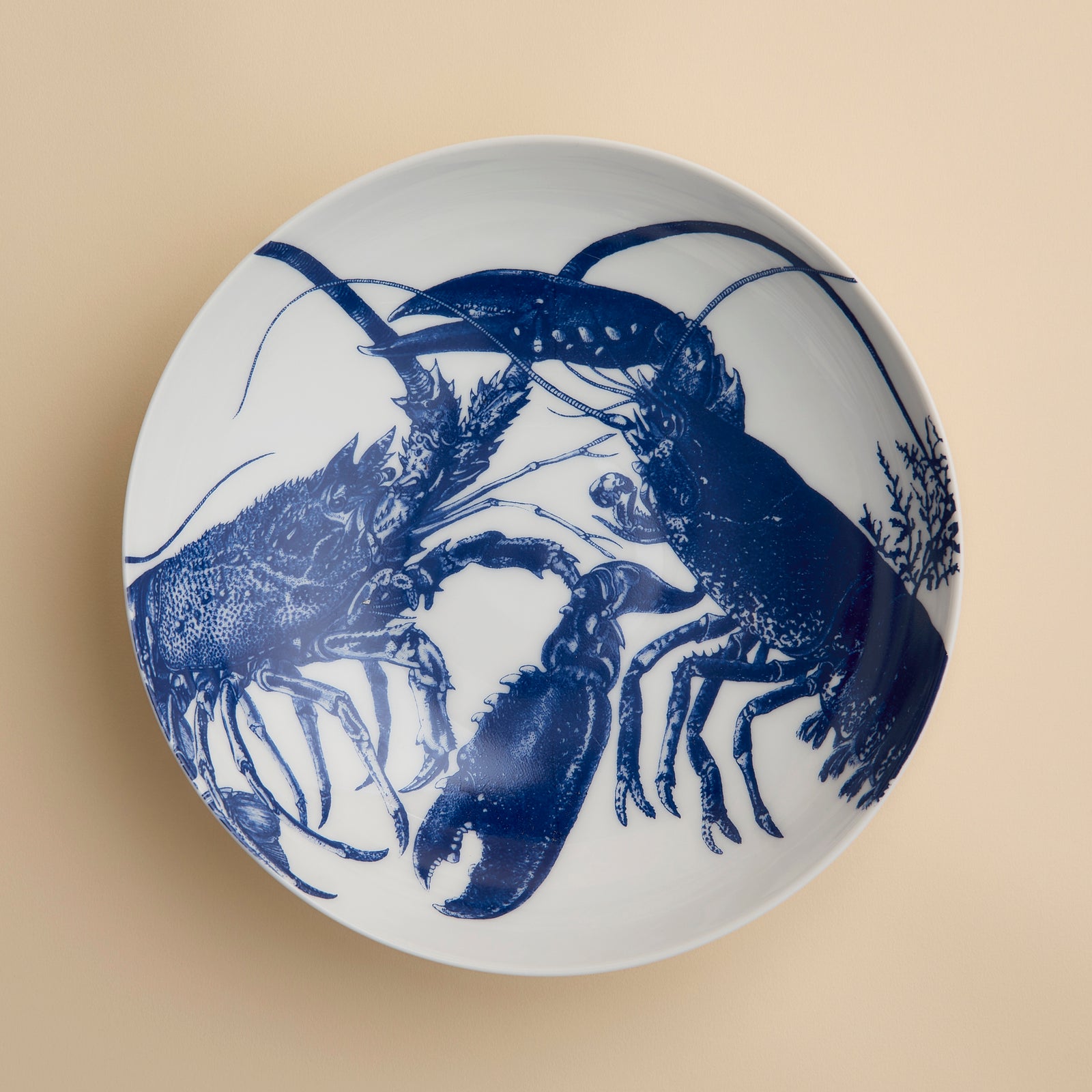 The Lobster Entrée Bowl by Caskata, from our coastal dinnerware collection, is a white ceramic bowl featuring a blue illustration of two lobsters facing each other on a beige background.