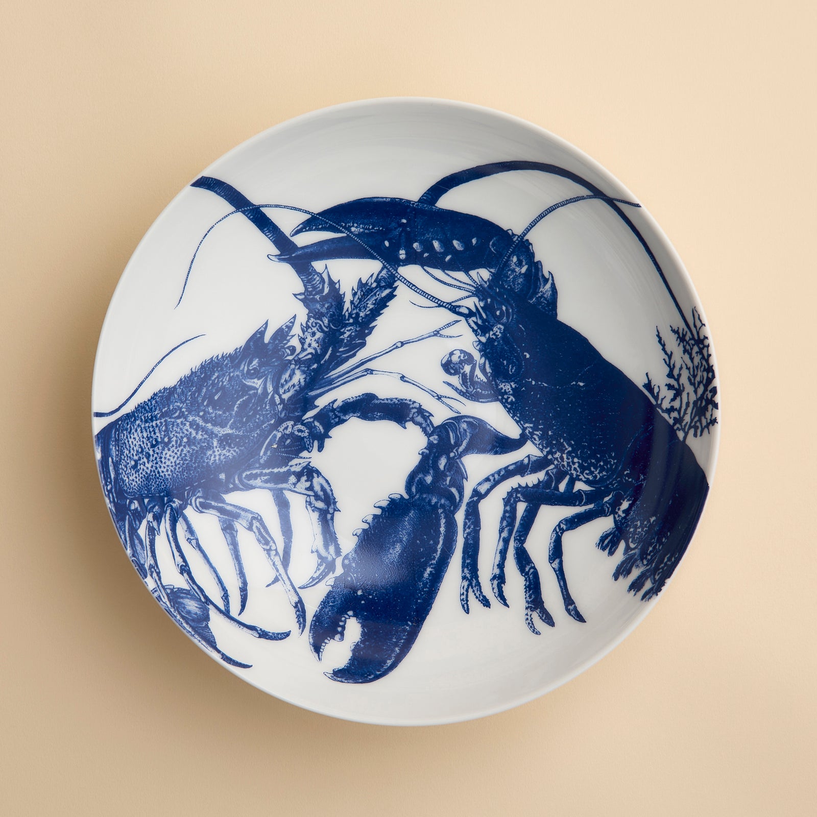The Lobster Entrée Bowl by Caskata, from our coastal dinnerware collection, is a white ceramic bowl featuring a blue illustration of two lobsters facing each other on a beige background.