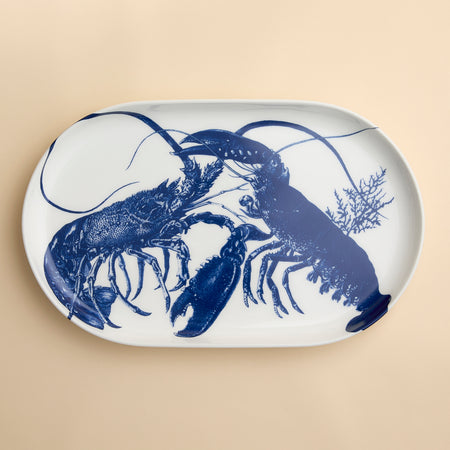 The Caskata Lobster Large Coupe Oval Platter features detailed blue lobsters with seaweed accents on white porcelain—a striking serving  piece in high-fired porcelain, perfect for entertaining.