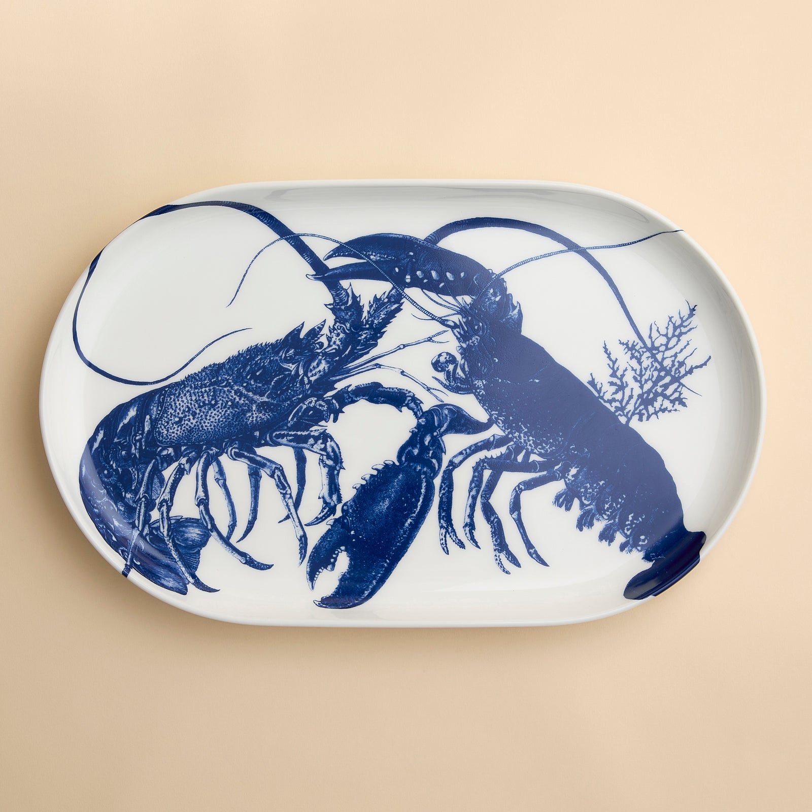 The Caskata Lobster Large Coupe Oval Platter features detailed blue lobsters with seaweed accents on white porcelain—a striking serving  piece in high-fired porcelain, perfect for entertaining.