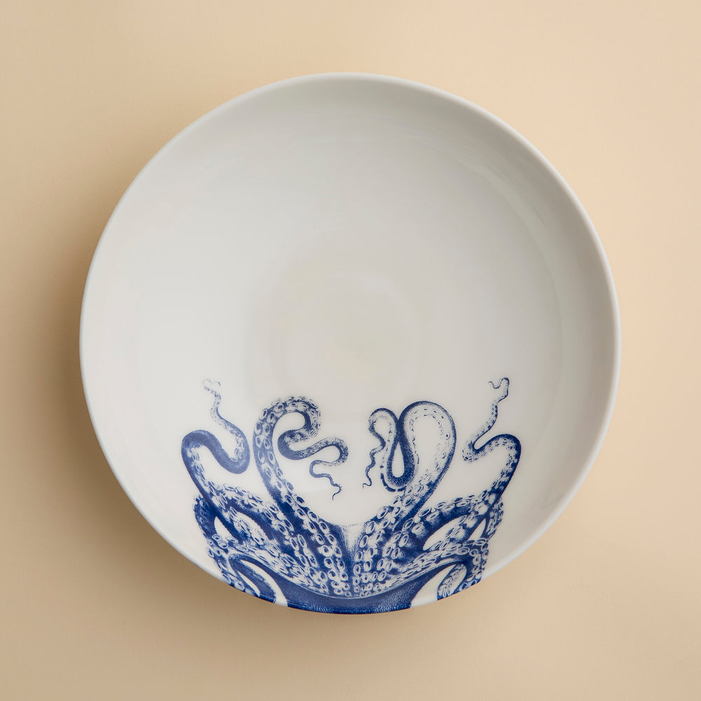 White ceramic plate featuring a blue octopus tentacle design on one side, set atop a beige surface—a striking piece that pairs beautifully with the Lucy Entrée Bowl by Caskata Artisanal Home or any other blue and white bowl in your collection.