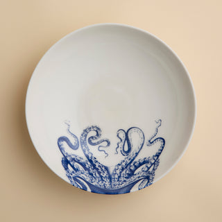 White ceramic plate featuring a blue octopus tentacle design on one side, set atop a beige surface—a striking piece that pairs beautifully with the Lucy Entrée Bowl by Caskata Artisanal Home or any other blue and white bowl in your collection.