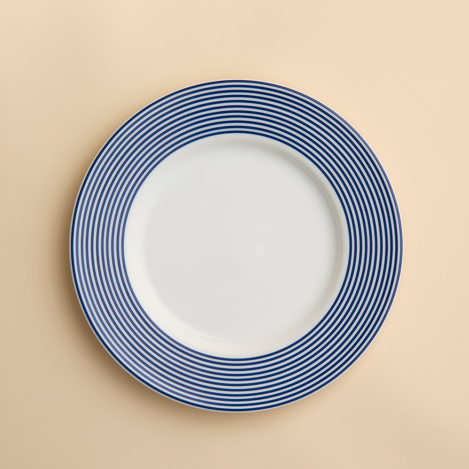Newport Stripe Rimmed Salad Plate crafted from high-fired porcelain featuring a Newport Stripe design with blue concentric circles around the rim by Caskata Artisanal Home. Shown against a creamy beige background.
