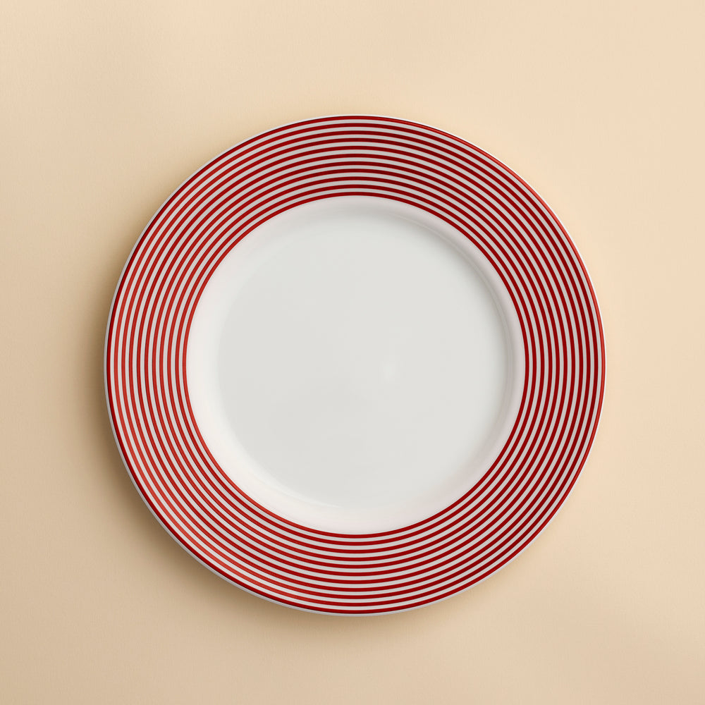 A Newport Crimson Stripe Salad with concentric rings of red stripes around the rim of this high-fired porcelain plate from Caskata, shown against a creamy beige background.