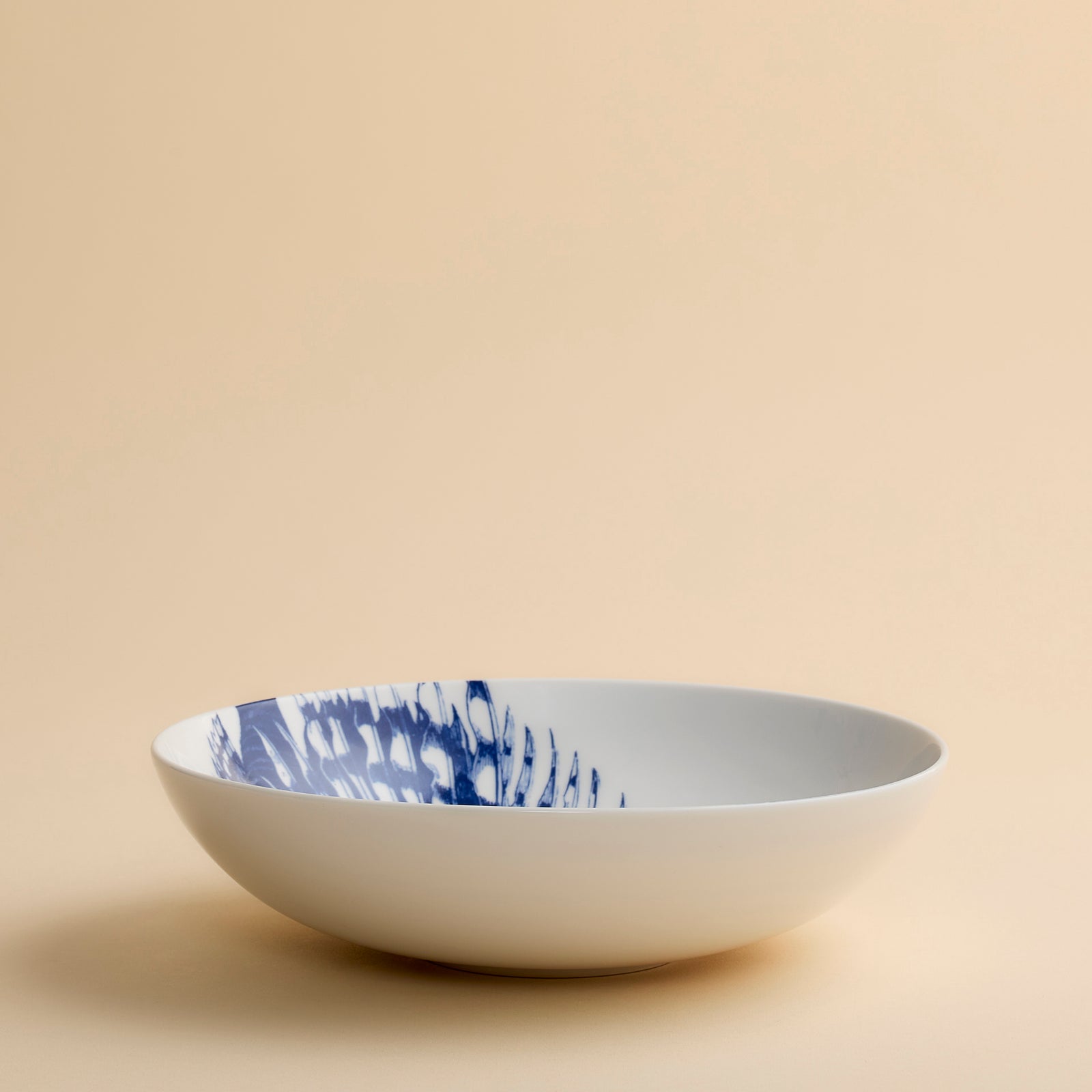 The Spiky Fish Entrée Bowl by Caskata features two blue fish illustrations facing each other on a white ceramic base, set against a plain beige background. Perfect for lovers of coastal dinnerware, this bowl adds a hint of maritime charm to any table setting.