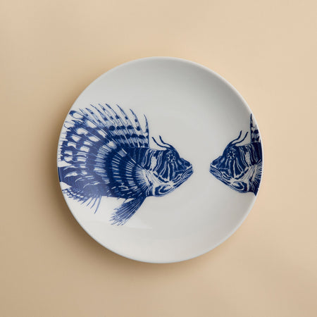 Add a playful coastal vibe to your dining table with the Caskata Spiky Fish Coupe Salad Plate—this white porcelain plate features two blue fish illustrations facing each other and is perfect for enhancing your coastal dinnerware collection.