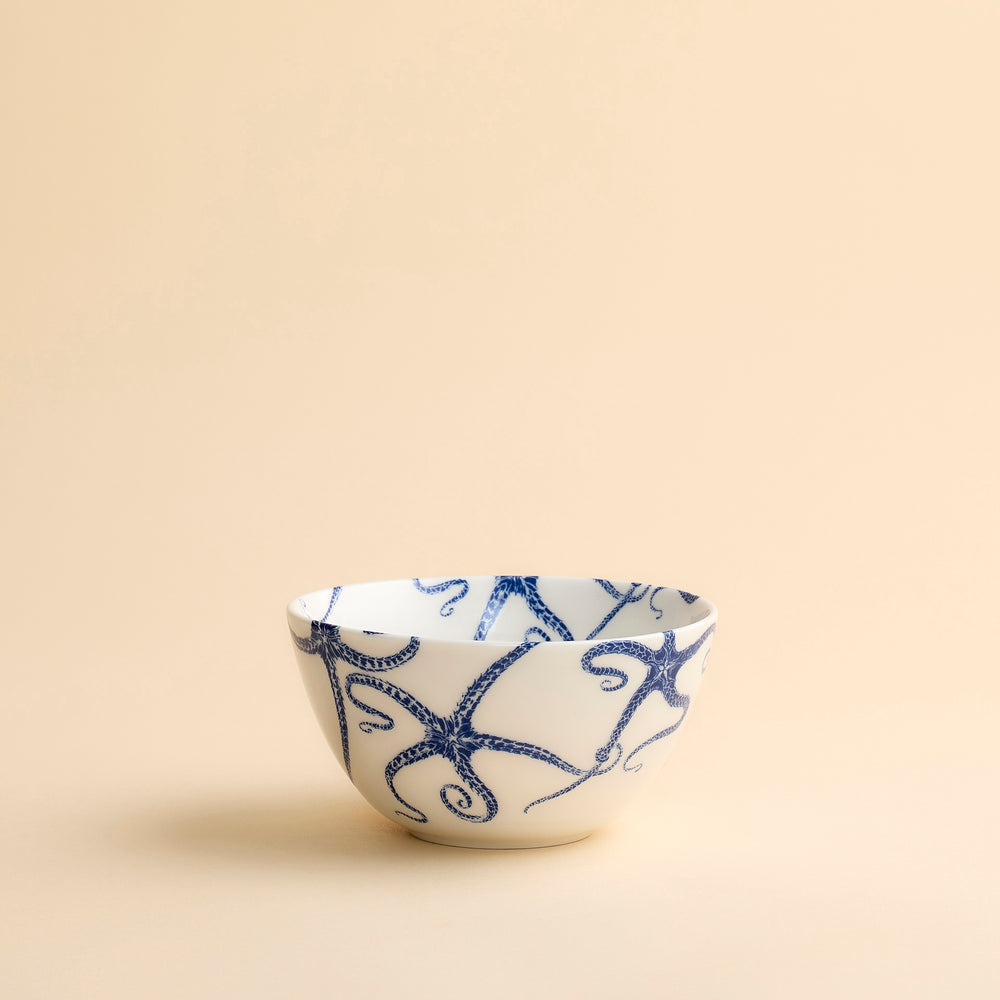 Whimsical Starfish Cereal Bowl with blue starfish dancing across creamy white porcelain from Caskata shown in profile on a beige background