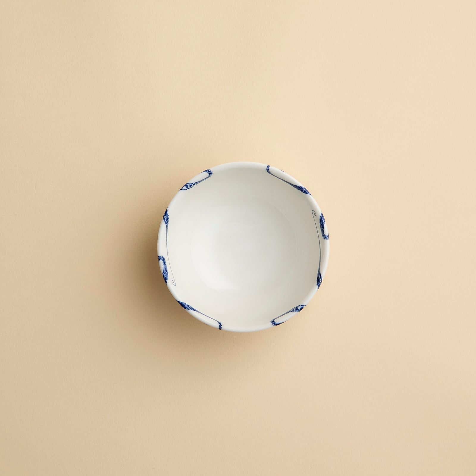 Whimsical Starfish Snack Bowl with blue starfish dancing across creamy white porcelain from Caskata shown in profile on a creamy beige background