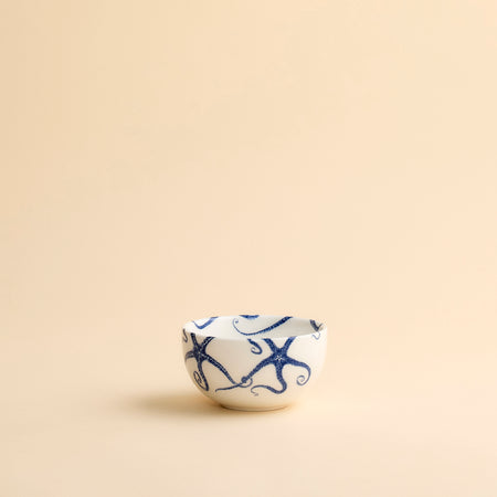 Whimsical Starfish Snack Bowl with blue starfish dancing across creamy white porcelain from Caskata shown in profile on a creamy beige background