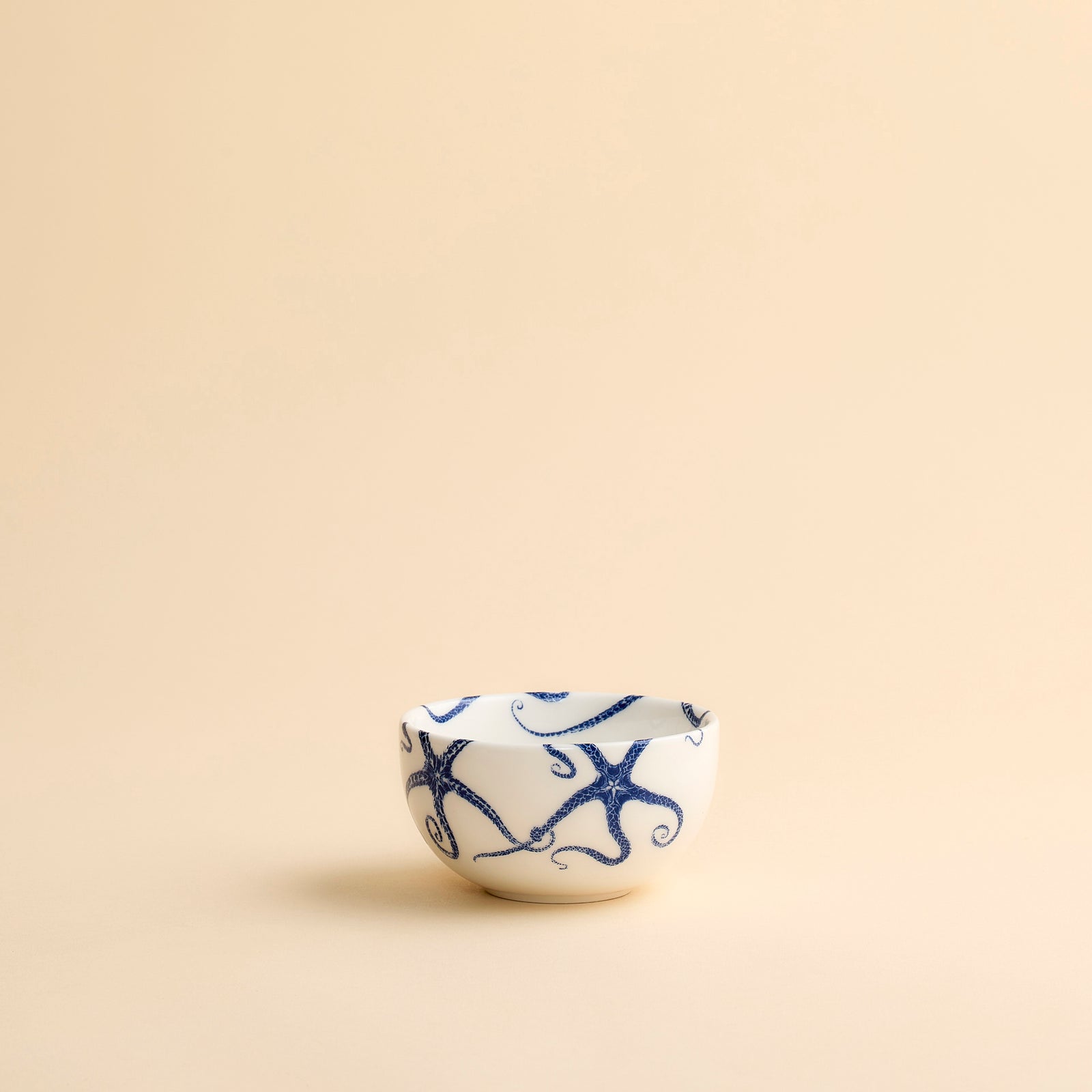 Whimsical Starfish Snack Bowl with blue starfish dancing across creamy white porcelain from Caskata shown in profile on a creamy beige background