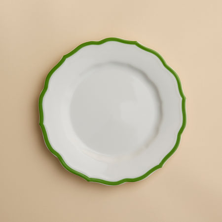 The Caskata Stella Scalloped Verde Salad Plate features high-fired porcelain with a scalloped green rim, shown from above on a beige background. This plate adds elegant, vintage-inspired charm to any table setting.