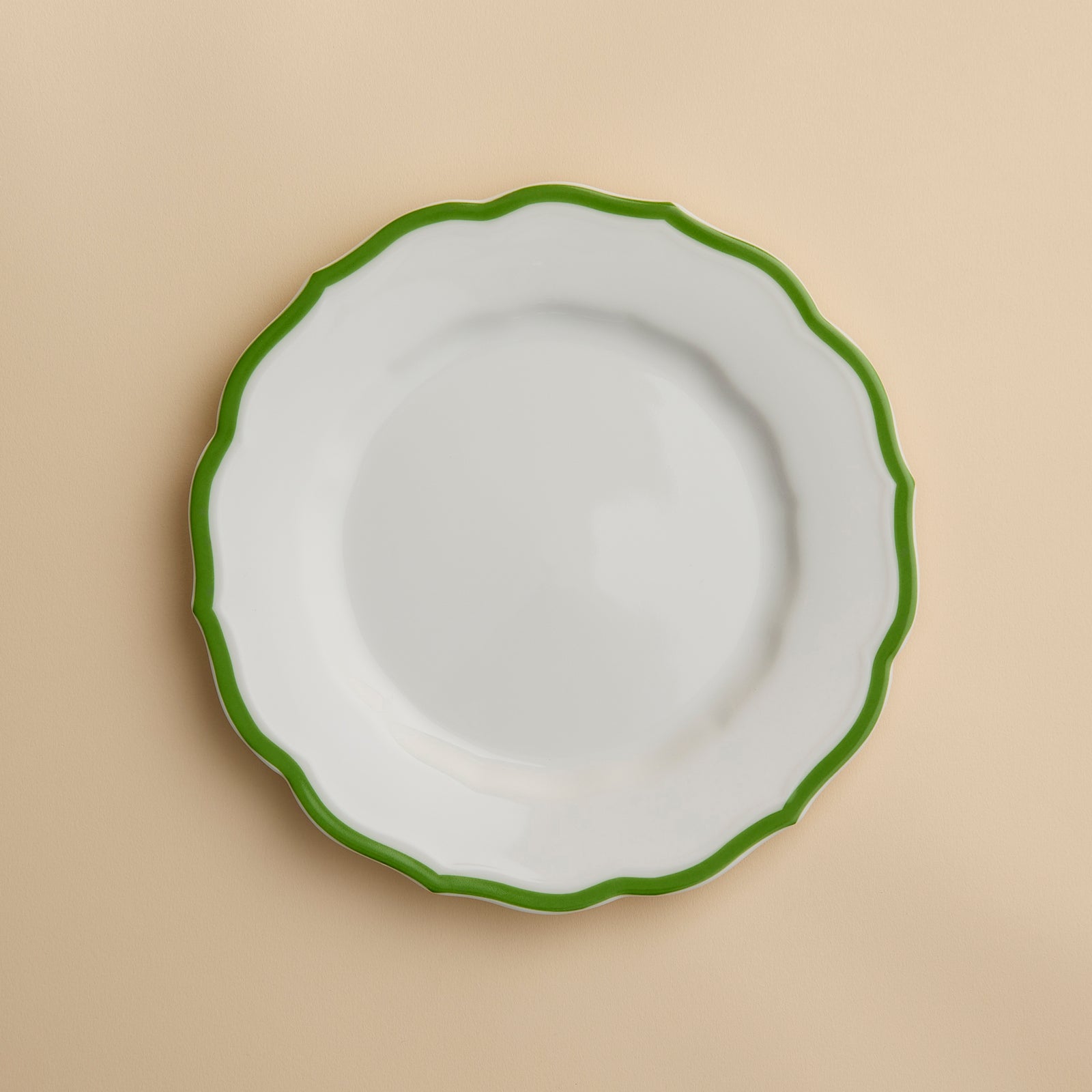 The Caskata Stella Scalloped Verde Salad Plate features high-fired porcelain with a scalloped green rim, shown from above on a beige background. This plate adds elegant, vintage-inspired charm to any table setting.