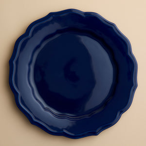 A round, dark blue Caskata Stella Scalloped Solid Blue Dinner Plate with a scalloped edge.