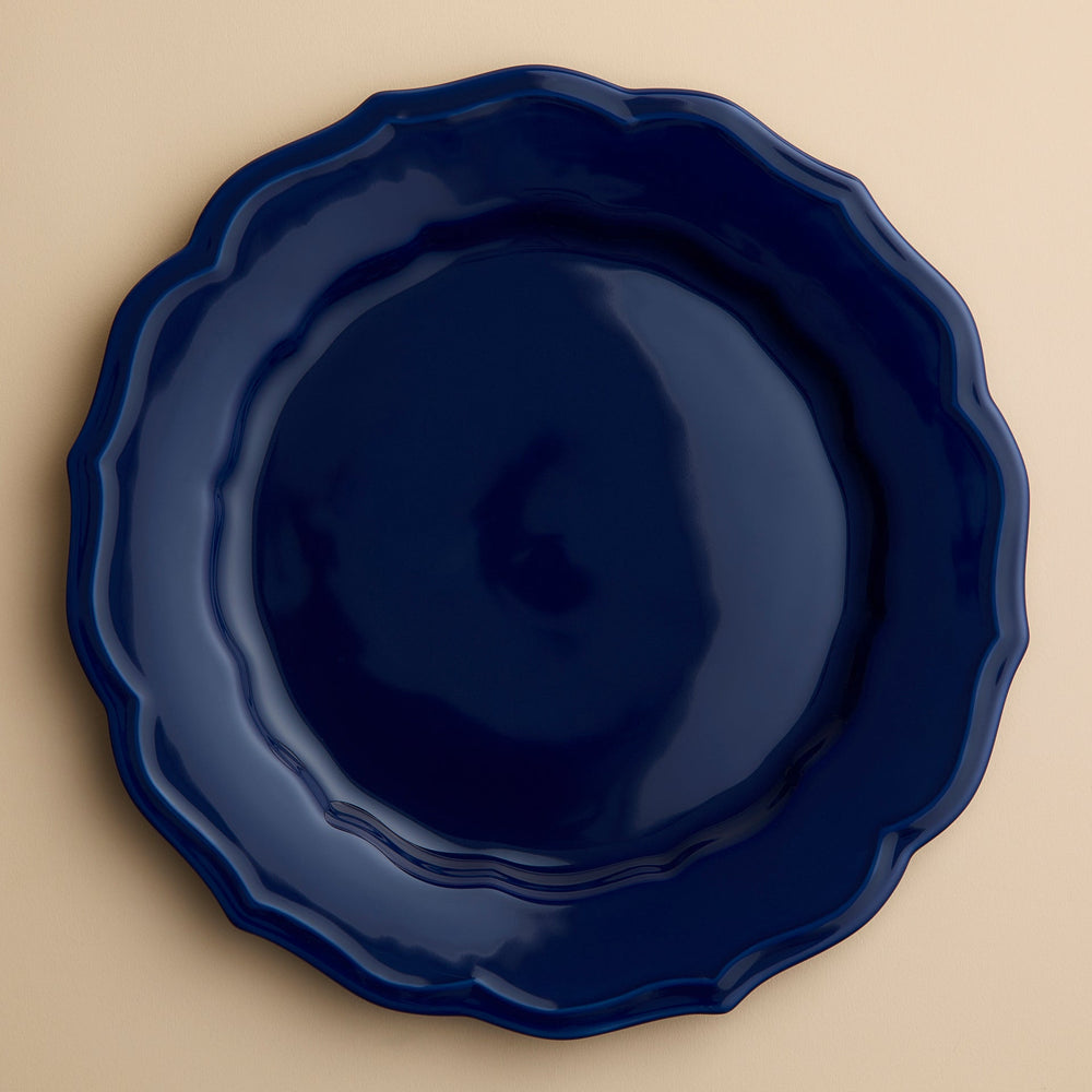 A round, dark blue Caskata Stella Scalloped Solid Blue Dinner Plate with a scalloped edge.