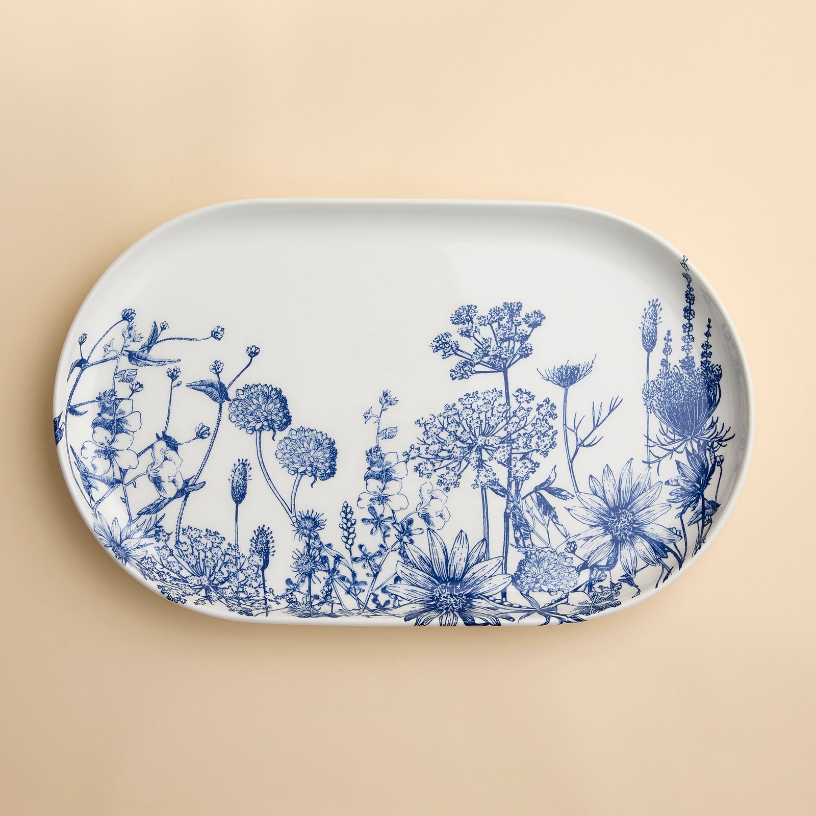 The Summer Blues Large Coupe Oval Platter by Caskata showcases exquisite blue floral illustrations on a creamy background and is crafted from high-fired porcelain.