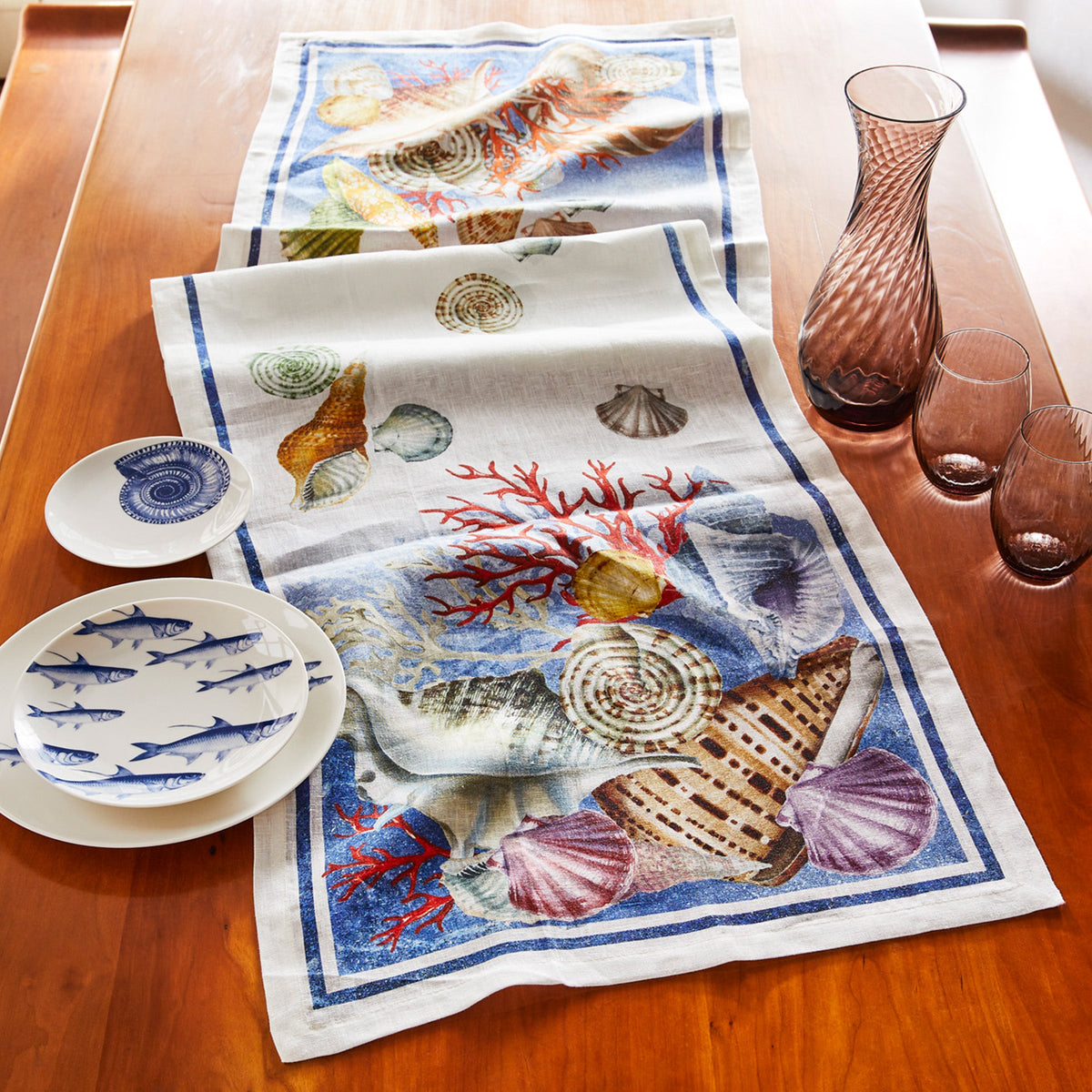 A Sanibel Linen Table Runner inspired by watercolor, featuring delicate sea shells. Ideal for adding a touch of coastal charm to your dining table. Perfect for shell collecting enthusiasts looking to enhance their home decor with TTT brand.