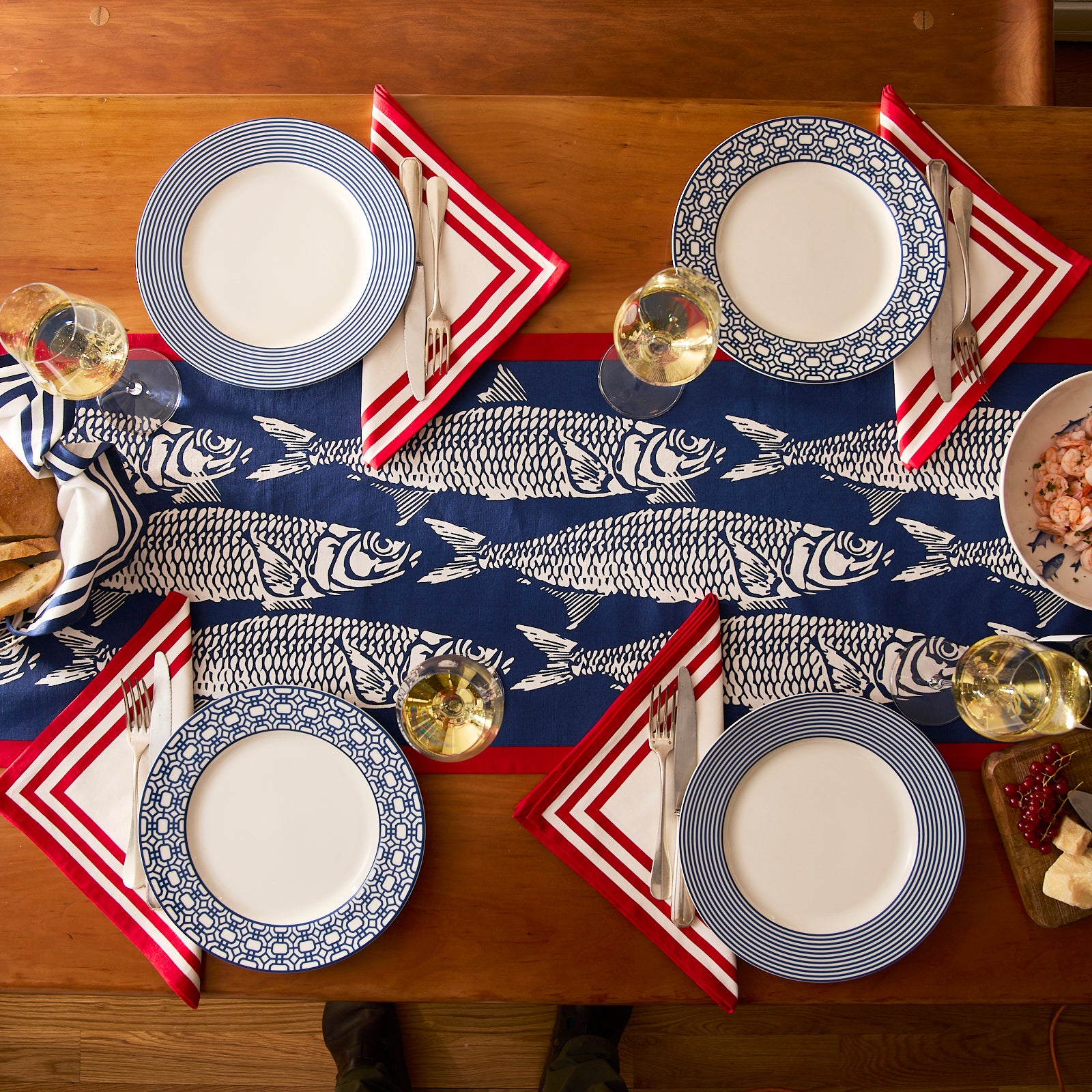 Two folded Caskata Sardines Table Runners, each with blue, white, and red fish designs, labeled 16" x 72" and 16" x 108".