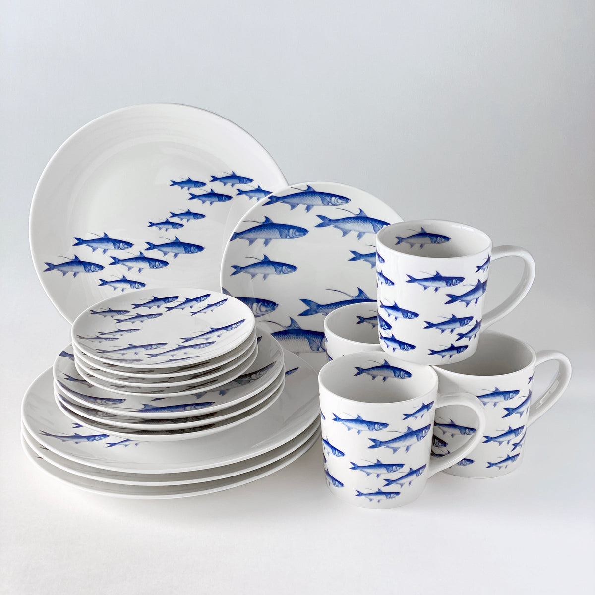 A **School of Fish Mug** in blue and white dinnerware set with sharks on it by Caskata Artisanal Home.