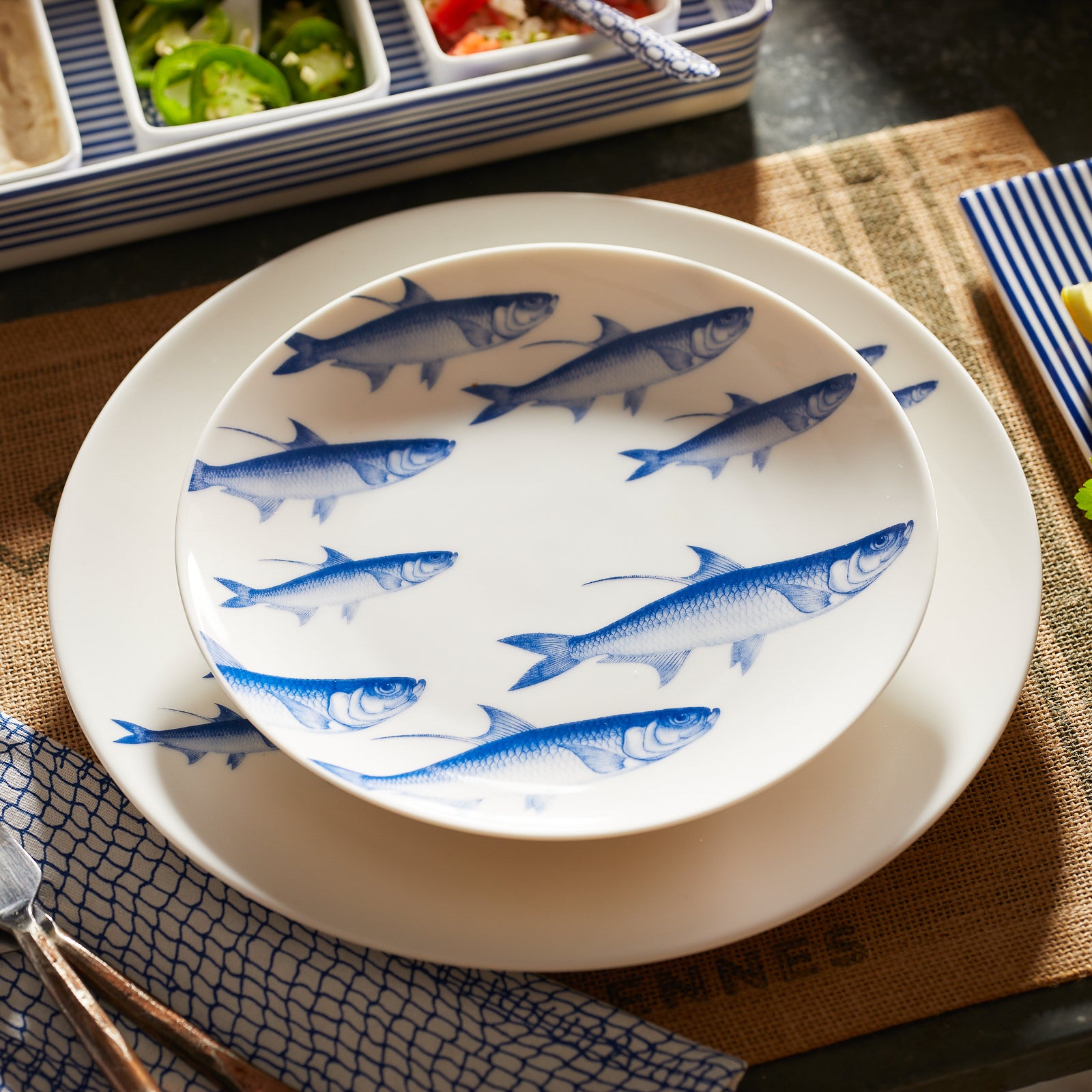 The Caskata School of Fish Table for 4 is a porcelain dinnerware set with blue fish on white, including 4 plates, 4 side plates, and 4 bowls. All pieces are dishwasher and microwave safe for everyday convenience.
