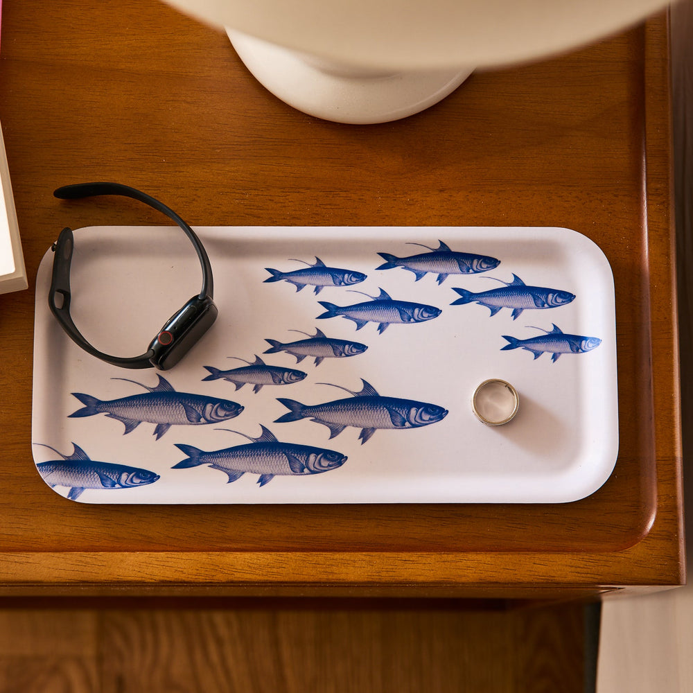 A watch and a ring sit elegantly on a Caskata School of Fish Small Rectangular Birchwood Tray, resting on a wooden surface.