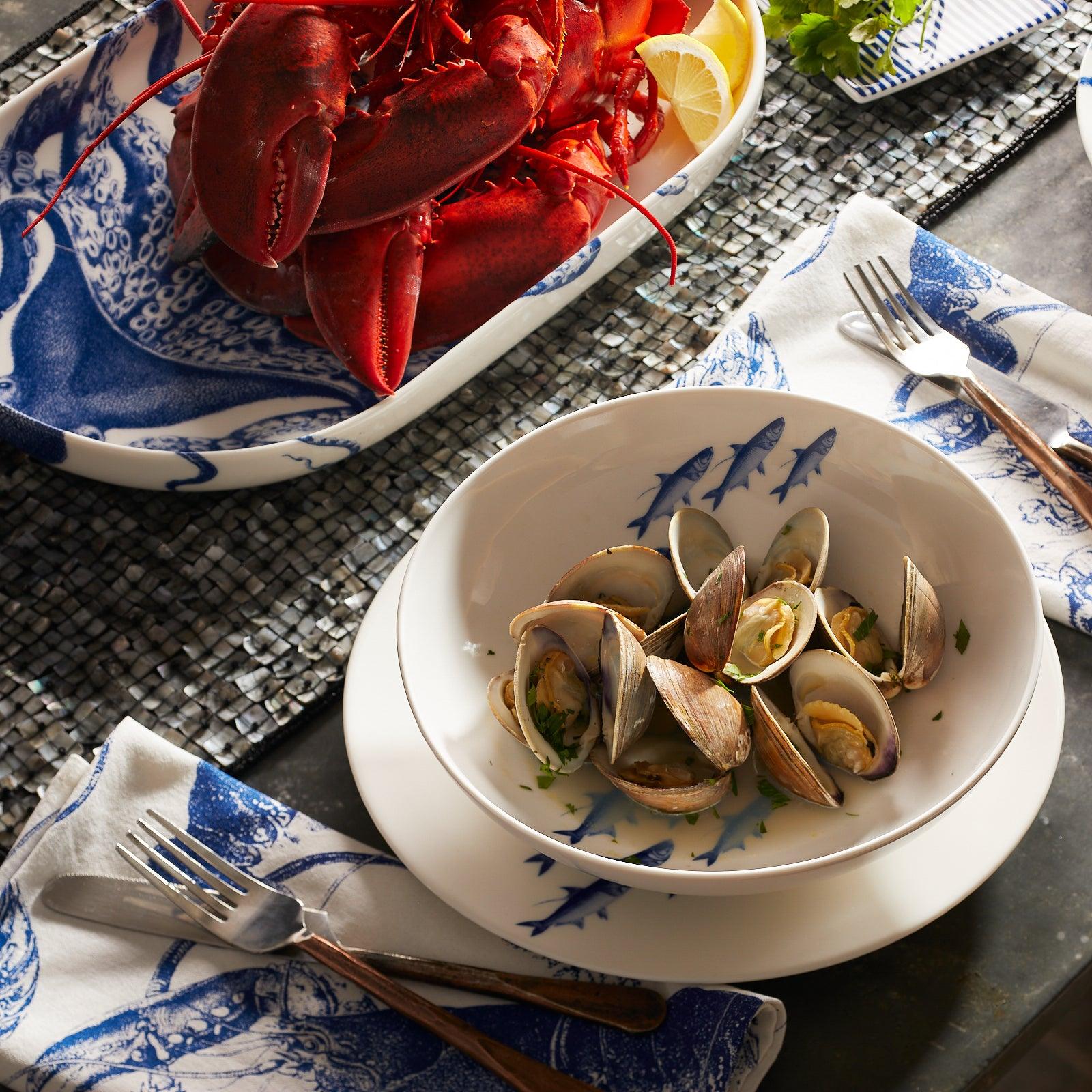 A Caskata Artisanal Home School Fish Entrée Bowl, decorated with a school of blue fish in the center, perfect for any dinnerware collection.